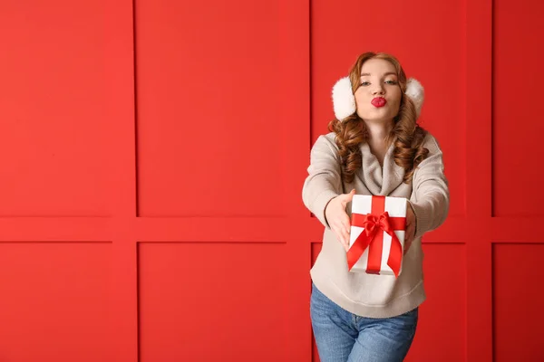 Happy young woman in winter clothes and with Christmas gift on color background — Stock Photo, Image