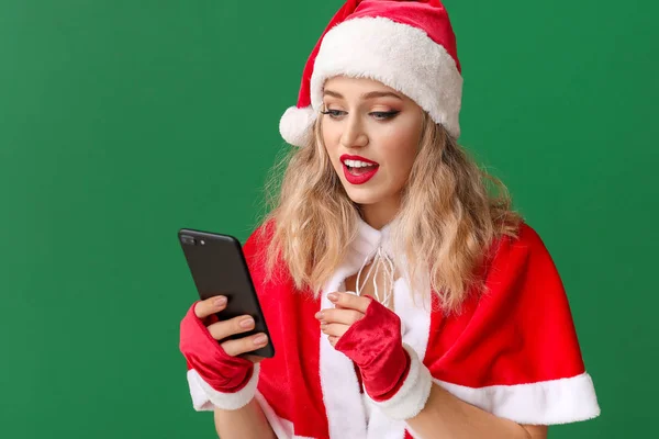 Beautiful young woman dressed as Santa with mobile phone on color background — Stock Photo, Image