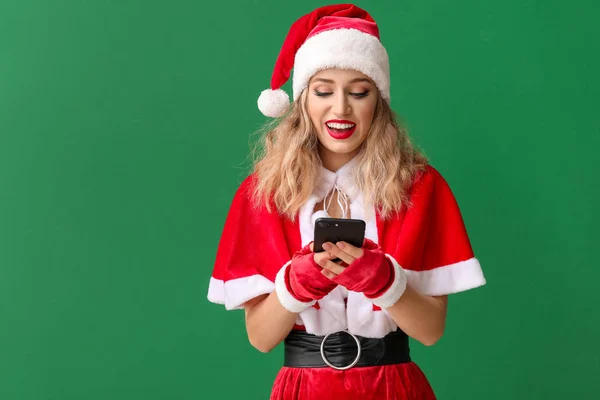 Beautiful young woman dressed as Santa with mobile phone on color background — Stockfoto