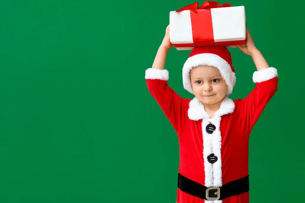 Cute little boy in Santa costume and with Christmas gift on color background — Stock Photo, Image