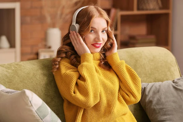 Mujer joven feliz en ropa de invierno escuchando música en el sofá en casa —  Fotos de Stock