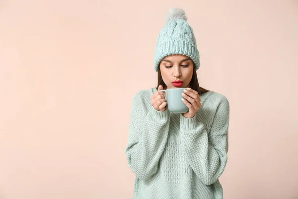 Jonge vrouw in winterkleding en met kopje thee op lichte achtergrond — Stockfoto