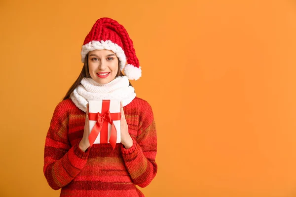 Happy young woman in winter clothes and with Christmas gift on color background — Stock Photo, Image