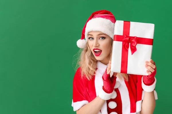Verrast jonge vrouw verkleed als kerstman met kerstcadeau op kleur achtergrond — Stockfoto