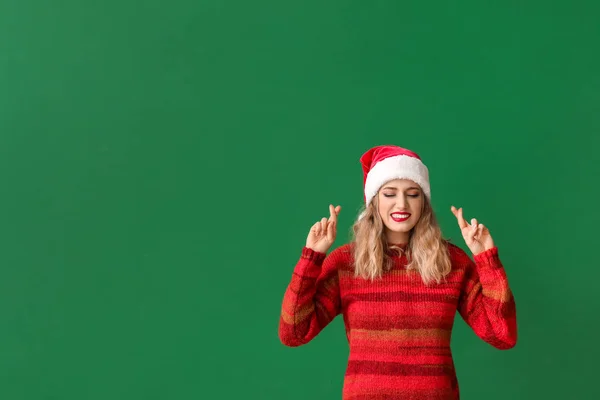 Beautiful young woman in Santa hat crossing fingers on color background — Stockfoto