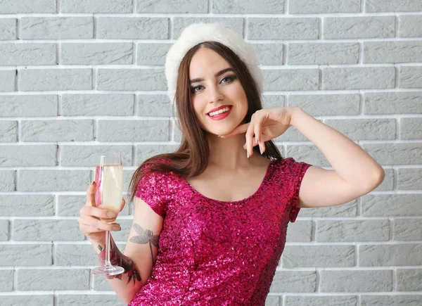 Piękna młoda kobieta w kapeluszu Santa i szampana na tle cegły — Zdjęcie stockowe