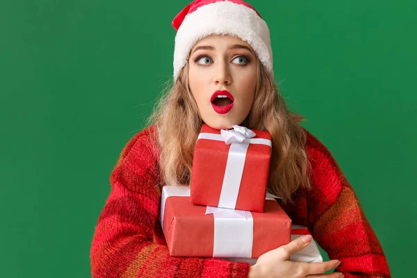 Surprise jeune femme dans le chapeau de Père Noël et avec des cadeaux de Noël sur fond de couleur — Photo