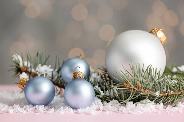Mooie kerstballen met sneeuw en sparren takken op tafel tegen wazig licht — Stockfoto