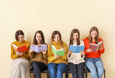 Kitapları olan genç kadınlar renk duvarının yanında oturuyor.