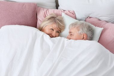 Mutlu olgun çift yatakta battaniyenin altında yatıyor.