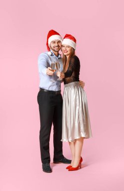 Noel Baba şapkalı mutlu çift ve renkli arka planda şampanya kadehleri
