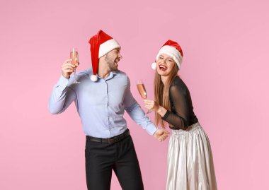 Noel Baba şapkalı mutlu çift ve renkli arka planda şampanya kadehleri