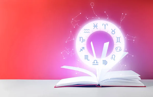 Astrological signs and open book on table against color background — Stock Fotó