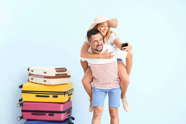 Couple with suitcases taking selfie on color background — Stock Photo, Image