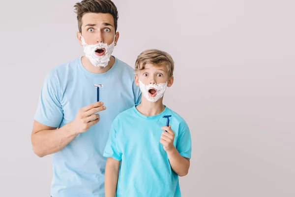 Αστείος πατέρας και ο μικρός γιος του ξυρίζονται σε γκρι φόντο. — Φωτογραφία Αρχείου