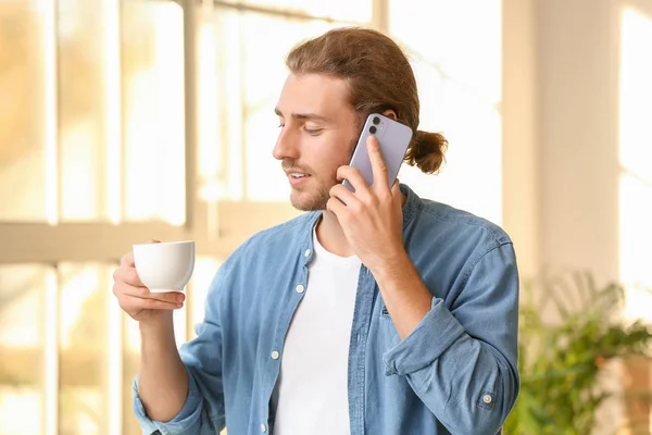 Przystojny mężczyzna z filiżanką kawy rozmawia przez telefon komórkowy w domu — Zdjęcie stockowe