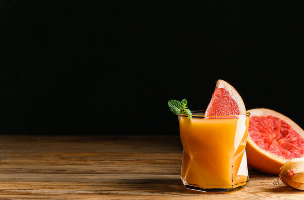 Glass of fresh juice and grapefruit on table against dark background