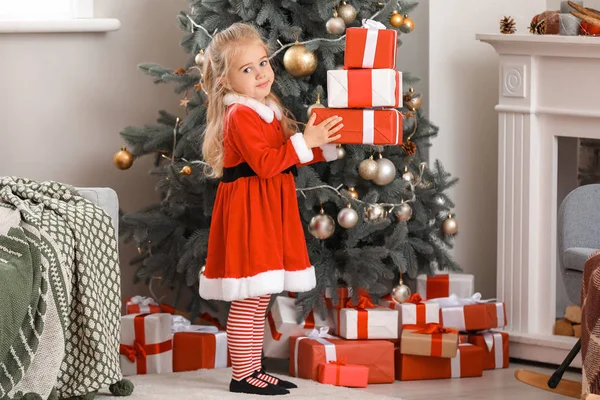 Petite fille mignonne en costume de Père Noël et avec des cadeaux de Noël à la maison — Photo