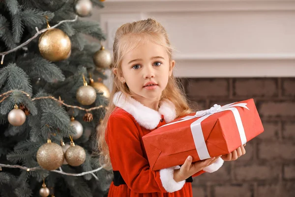 Cute little girl w stroju Mikołaja i z prezentem świątecznym w domu — Zdjęcie stockowe