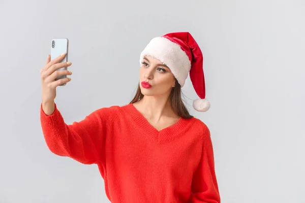 Noel Baba şapkalı güzel genç bir kadın arka planda selfie çekiyor. — Stok fotoğraf