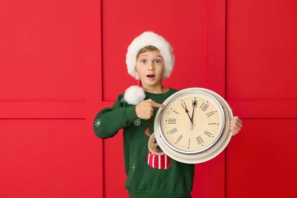 Überraschte kleine Junge mit Uhr auf farbigem Hintergrund. Weihnachts-Countdown-Konzept — Stockfoto