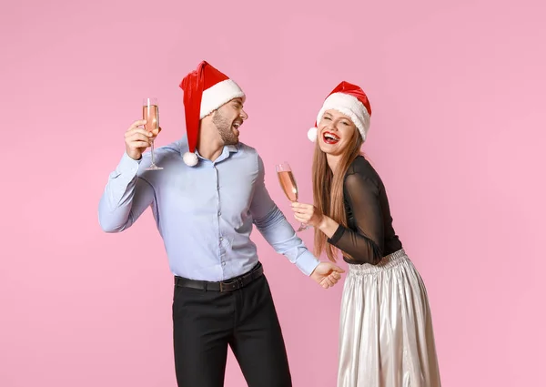 Casal feliz em chapéus de Papai Noel e com copos de champanhe no fundo de cor — Fotografia de Stock