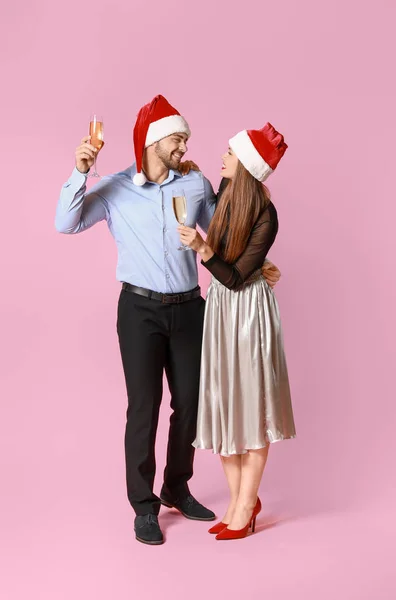 Casal feliz em chapéus de Papai Noel e com copos de champanhe no fundo de cor — Fotografia de Stock