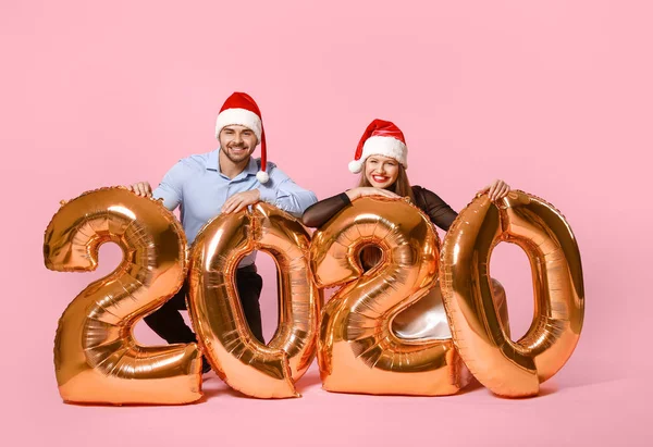 Gelukkig paar in Santa Claus hoeden en met luchtballonnen op kleur achtergrond — Stockfoto