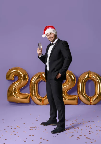 Bello giovanotto in cappello Babbo Natale e con bicchiere di champagne su sfondo a colori — Foto Stock