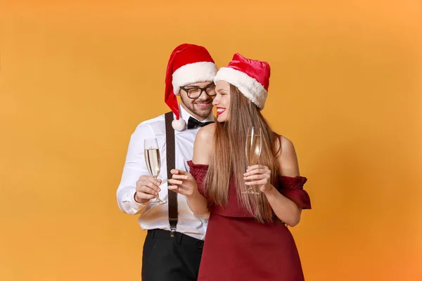 Happy young couple in Santa Claus hats and with glasses of champagne on color background — Stock Photo, Image