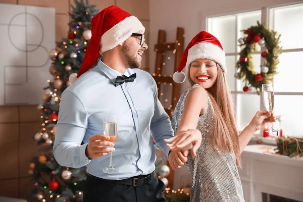 Happy young couple in Santa Claus hats and with glasses of champagne at home — Stock Photo, Image