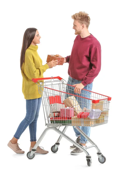 Young couple with shopping cart full of Christmas gifts on white background — Stock Photo, Image