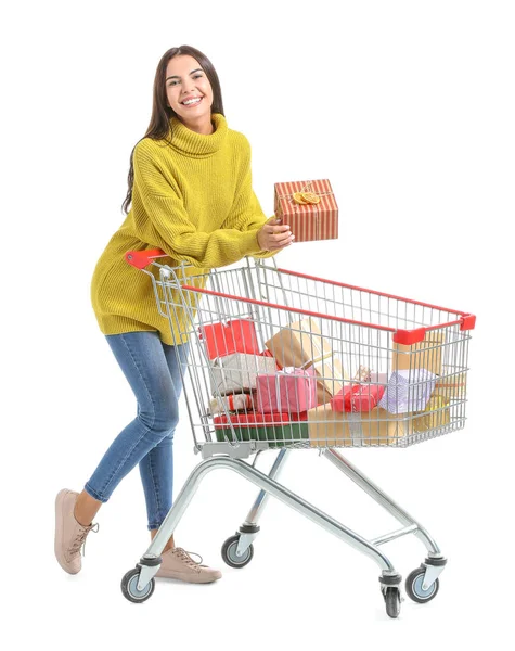 Young woman with shopping cart full of Christmas gifts on white background — Stock Photo, Image