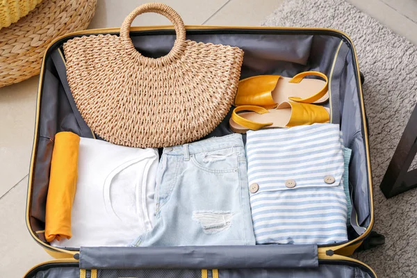 Open suitcase with packed clothes on floor at home — Stock Photo, Image