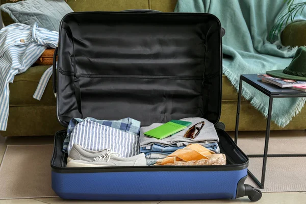 Open suitcase with packed clothes and accessories on floor at home