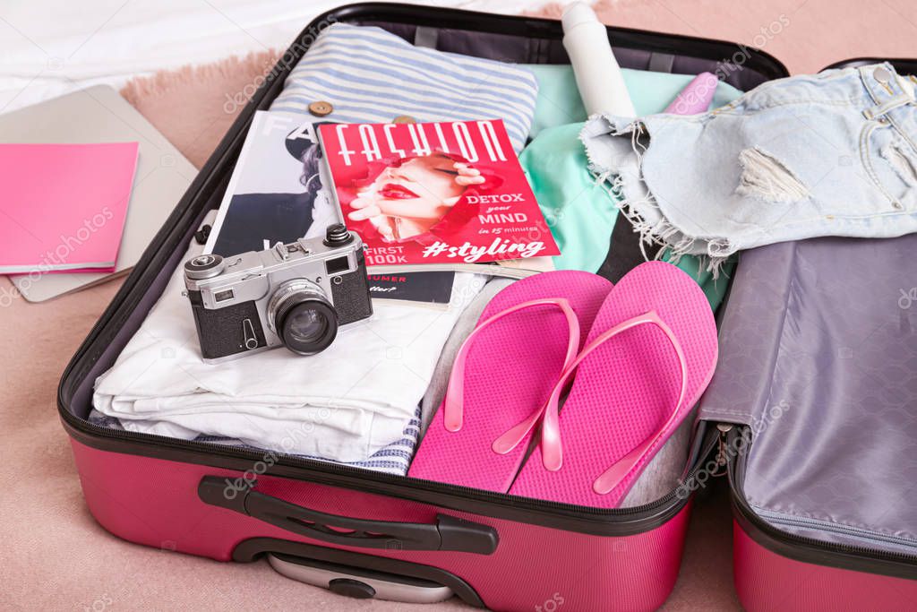Open suitcase with packed clothes and accessories on bed