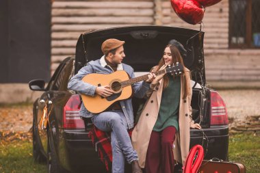 Arabası ve gitarıyla parkta dinlenen mutlu genç bir çift. Sevgililer Günü kutlaması
