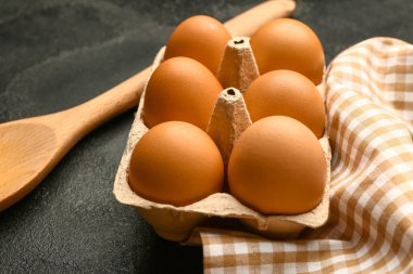 Koyu arkaplanda taze yumurta ve kaşık paketi var.