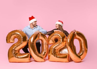 Noel Baba şapkalı mutlu çift ve renkli balonları var.