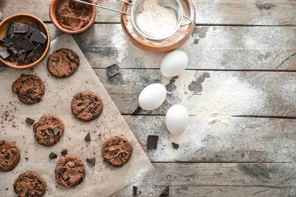 Tasty chocolate chip cookies with flour and eggs on wooden background — Stock Photo, Image