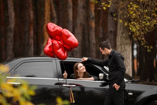 Mann in der Nähe seiner Freundin mit Luftballons im Auto. Valentinstag-Feier — Stockfoto