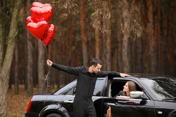 Человек с воздушными шарами рядом со своей девушкой сидит в машине. Празднование Дня Святого Валентина — стоковое фото