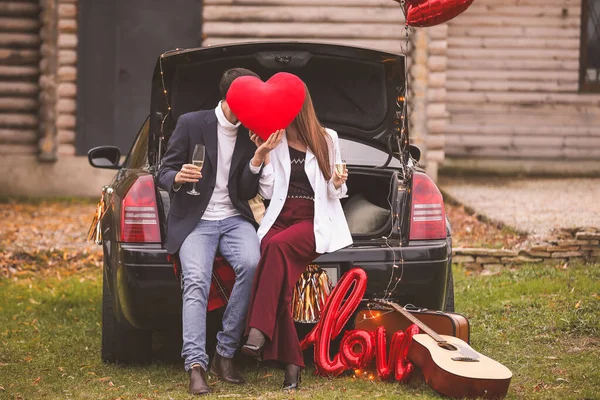 Pasangan muda bahagia dengan mobil dan, sampanye dan jantung di taman. Hari Valentine perayaan — Stok Foto