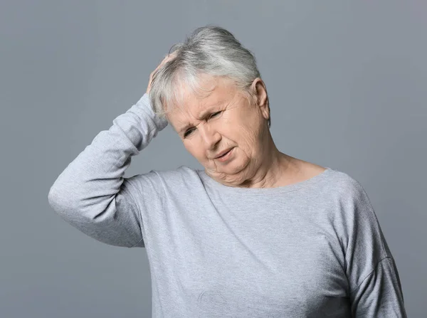 Seniorin leidet unter Kopfschmerzen auf grauem Hintergrund — Stockfoto