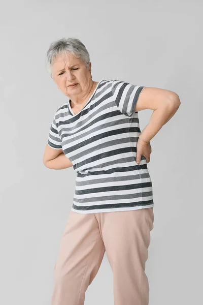 Senior vrouw die lijden aan rugpijn op grijze achtergrond — Stockfoto