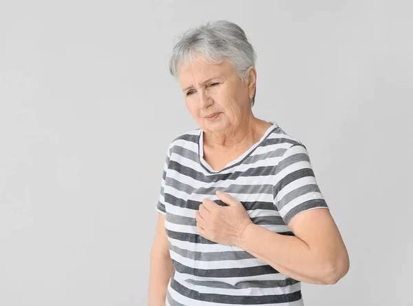 Senior woman suffering from heart attack on grey background — Stock Photo, Image