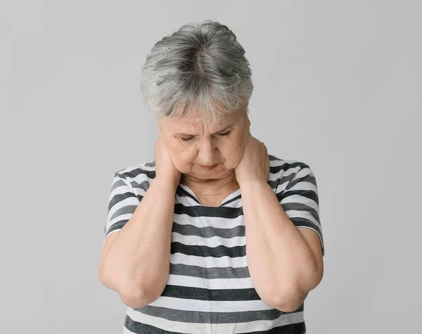 Старша жінка, яка страждає від болю в шиї на сірому фоні — стокове фото
