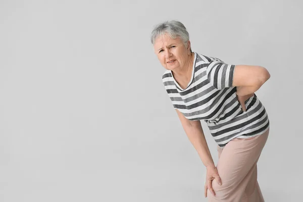 Старша жінка, яка страждає від болю в спині на сірому фоні — стокове фото