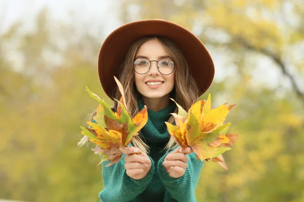 Portrait of stylish young woman with autumn leaves outdoors — Stock Photo, Image