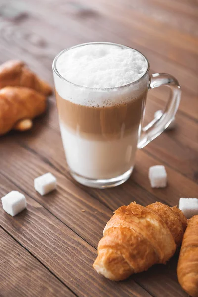 Skleněný šálek chutného latté s croissanty na dřevěném stole — Stock fotografie